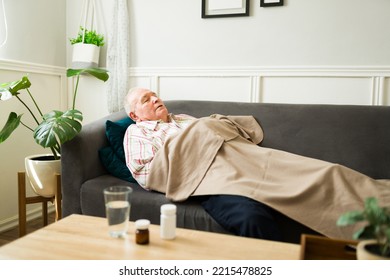 Tired Senior Caucasian Man Feeling Sick Sleeping On The Sofa With A Blanket And Resting In The Living Room