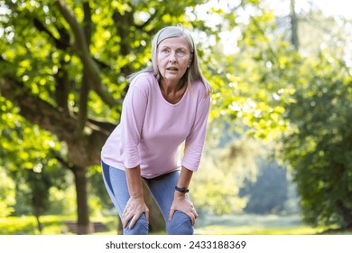 Tired senior gray-haired woman doing sports, jogging and walking in the park, standing with hands on knees and resting, breathing heavily. - Powered by Shutterstock