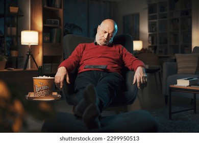 Tired senior man falling asleep in front of the TV late at night with the remote control on his belly - Powered by Shutterstock