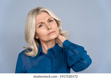 Tired sick older middle aged 50s business woman rubbing neck feeling discomfort neck pain isolated on grey background. Stressed old mature lady suffering from neckpain massaging sore back muscles.