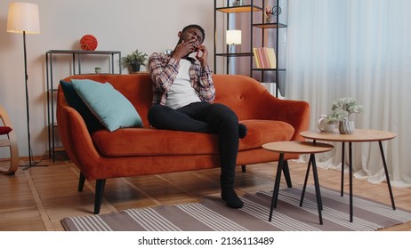 Tired Sleepy Casual Man In Shirt Talking On Mobile Phone With Friend At Home. Sad African American Guy Freelancer Making Online Conversation Speaks On Smartphone Sitting Alone On Sofa At Living Room