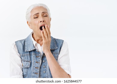 Tired sleepy old lady wake-up early and yawning, cover opened mouth with palm close eyes, feeling slight fatigue, dreaming sip of coffee, standing bored and indifferent white background - Powered by Shutterstock