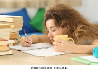 Tired and sleepy student with tousled hair trying to write notes on a desk in her room in a house indoor