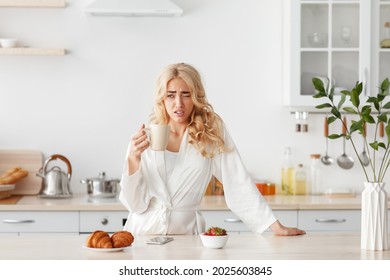 Tired Sleepy Woman Eating Breakfast Alone, Facial Emotions, Insomnia And Sleeping Disorder. Sad Millennial Beautiful Blonde Female Drinking Coffee In White Scandinavian Kitchen Interior, Empty Space