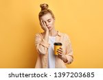 Tired sleepy woman holds a cup of coffee, has sad expression, closes eyes, cannot wake up in the morning and go to work. difficult, hard monday. isolated yellow background