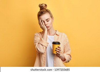 Tired sleepy woman holds a cup of coffee, has sad expression, closes eyes, cannot wake up in the morning and go to work. difficult, hard monday. isolated yellow background - Shutterstock ID 1397203685