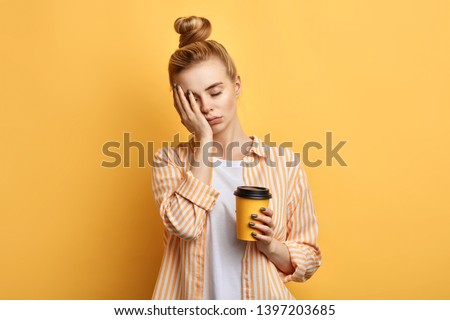 Tired sleepy woman holds a cup of coffee, has sad expression, closes eyes, cannot wake up in the morning and go to work. difficult, hard monday. isolated yellow background