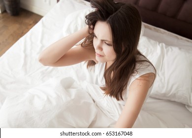 Tired sleepy woman with messy hair sitting in bed after wake up in the morning. Young female feeling exhausted after sleepless night. Insomnia, sleep disorder, headache or migraine, hangover concept 