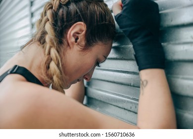 Tired sportswoman resting supported on a metal wall outdoors - Powered by Shutterstock