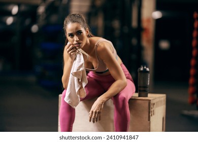 A tired sportswoman is wiping her sweat with towel while taking a break in a gym. - Powered by Shutterstock