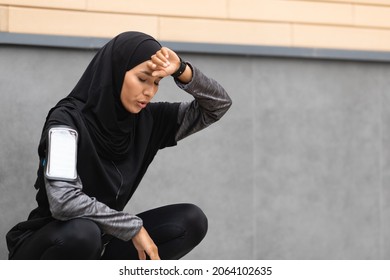 Tired Sporty Muslim Woman Taking Breath After Active Training Outdoors, Athletic Islamic Lady In Modest Sportswear Sitting Near Urban Wall, Resting After Jogging On City Street, Copy Space - Powered by Shutterstock