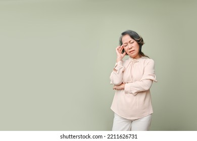 Tired and stressed 60s aged Asian woman in casual clothes touching her forehead, eyes closed, suffering from migraine or headache, standing over isolated green background. copy space for your text  - Powered by Shutterstock