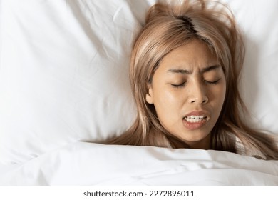Tired and stressed Asian woman with colored hair sleeping, having bad dream, nightmare with bruxism or grinding teeth