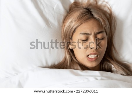 Tired and stressed Asian woman with colored hair sleeping, having bad dream, nightmare with bruxism or grinding teeth