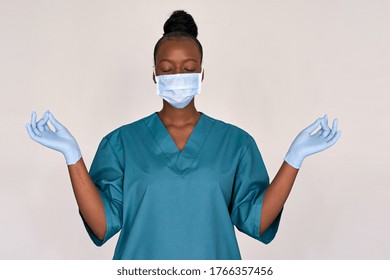 Tired stressed female african american scrub frontline nurse wear face mask blue uniform meditating on grey background. Black woman doctor eyes closed breathing doing yoga feels stress relief concept.