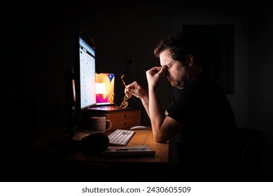 Tired and stressed office worker illuminated by the glow of their computer screen in a dark room at night while working late. Burn out. - Powered by Shutterstock