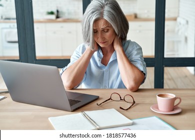 Tired stressed old mature business woman suffering from neckpain working from home office sitting at table. Overworked senior middle aged lady massaging neck feeling hurt pain from incorrect posture. - Shutterstock ID 1818577436