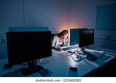 Tired and stressed out woman working late in an office, leaning at her desk and holding head in hands while looking at desktop computer screen - Shutterstock ID 2255602083