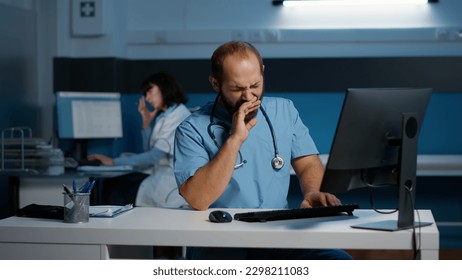 Tired stressed physician nurse working over hours at medical expertise in hospital office, typing patient report on computer. Assistant examining medication prescription. Health care service - Powered by Shutterstock