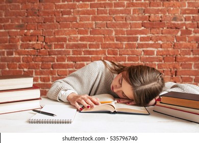 Tired student sleeping on book at library, free space. Exhausted of studying girl napping while reading tutorial material, copy space on brick wall background. Education, exams concept - Powered by Shutterstock