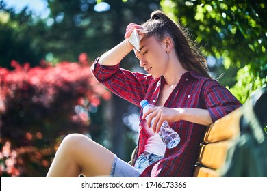 Tired Sweating Woman Wipes Her Forehead With A Napkin And Holds Cold Water Bottle In A Park In Summer Hot Weather