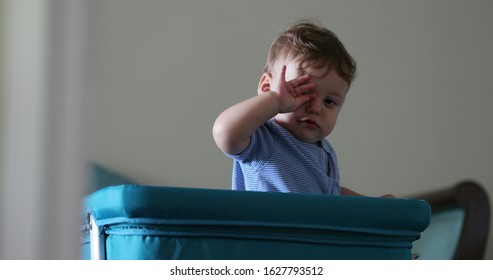 
Tired sweet baby peeking head from crib. Adorable toddler head appearing from cradle rubbing eye wanting to sleep