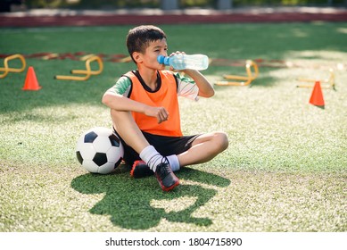 Tired teen boy in soccer uniform drinks with water from plastic bottle after intensive training at stadium in morning. - Powered by Shutterstock