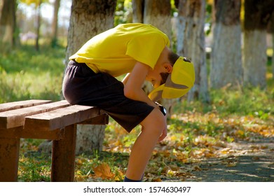 Tired Teen Boy In A Yellow Shirt And A Yellow Cap In The Park On A Bench.