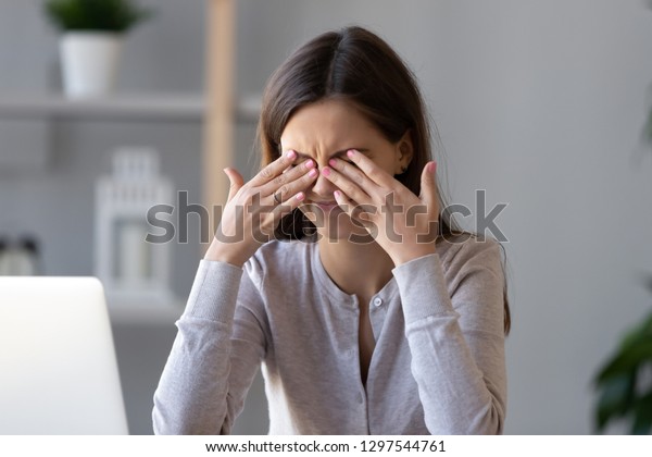 Tired teen girl rubbing dry irritable eyes feel\
eye strain tension migraine after computer work, exhausted young\
woman worker student relieving headache pain, bad weak blurry\
vision, eyesight problem