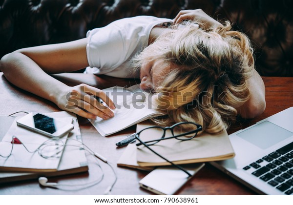 疲れた10代の女の子が 学校の宿題をしながらテーブルで寝ている 怠惰と先延ばしのコンセプト の写真素材 今すぐ編集