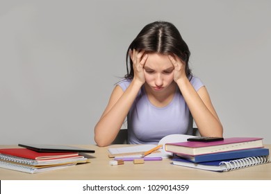 Tired Teenager Girl Doing Homework Against Grey Background