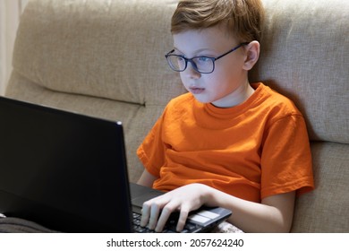 A Tired Teenager With Glasses Sits In The Dark At A Laptop And Does Homework Or Plays Computer Games.