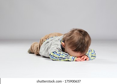 Tired toddler boy lying on the ground with his face down