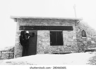 Tired Tourist With Backpack Is Knocking On Locked Door Of Stony Mountain Cottage. Winter In Mountains. Black And White Photo.