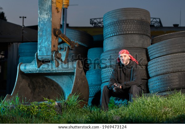 Tired tractor driver in bandana resting near tires\
at night