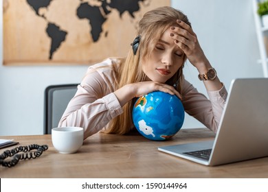 Tired Travel Agent Leaning On Globe While Sitting At Workplace With Closed Eyes