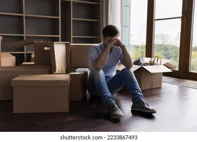 Tired unhappy bankrupt man moving out from apartment, sitting at pile of paper cardboard relocation boxes, waiting for delivery service, feeling headache, stress about eviction, divorce