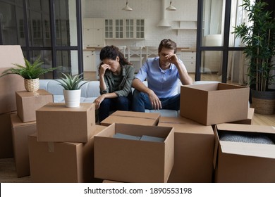 Tired Unhappy Young Caucasian Couple Sit On Sofa In New Living Room Feel Unmotivated Unpacking. Upset Stressed Millennial Man And Woman Have Fight Quarrel Unboxing Packages Relocating Moving.