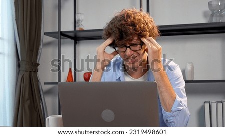 Tired unhappy young man wear eye glasses looking laptop headache depression worried problem  business online at home. Frightened businessman despair problems work loss job stress look at computer. 