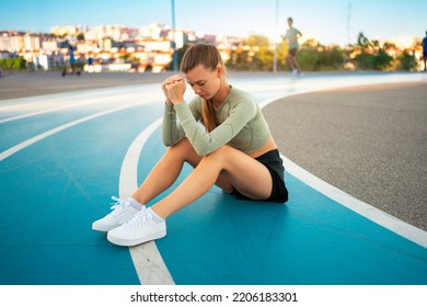 Tired Upset Female Athlete Sitting On Running Track Resting After Jogging Exercises. Disappointed Sport Result. Amateur Sprinter Sportswoman Exhausted After Tough Trainings Sitting On Track