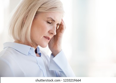 Tired Upset Mature Old Businesswoman Suffering From Strong Chronic Headache Migraine Or Memory Loss At Work, Stressed Dizzy Fatigued Middle Aged Senior Woman Office Worker Feels Pain In Aching Head