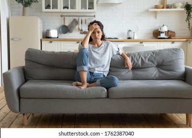 Tired Upset Woman Worried About Tiredness From Domestic Work Sitting At Couch. Frustrating Mom Stressful Feels Heaviness And Headache At Home. Fatigue Parent Trying Relaxing In Living Room.