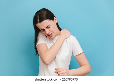 Tired upset young brunette woman massaging hurt stiff neck, fatigued sad brunette girl rubbing tensed muscles to relieve joint shoulder pain, isolated on blue studio background. Fibromyalgia concept - Shutterstock ID 2107939754