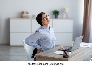 Tired Upset Young Indian Business Woman Suffering From Back Pain, Muscle Spasm At Workplace With Laptop In Office Or Home Interior. Fatigue, Deadline, Pain And Incorrect Posture, Work At Computer