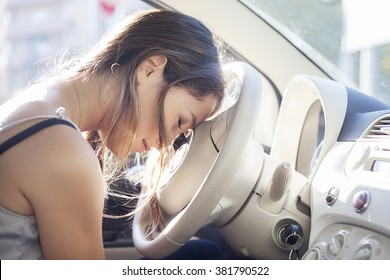 Tired woman asleep on steering wheel in her car