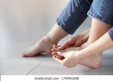 Tired woman doing self foot massage for pain relief after fatigue, long walking, working, standing, flat feet or injury, sitting indoors. Suffering from hurt of arch, ball, heel or toe treatment
