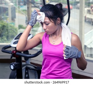 Tired Woman Drying His Sweaty Forehead With A Towel In The Gym. Sporting Woman Wiped The Sweat From His Brow In The Gym. Fatigue In The Gym. Training Woman In The Gym Wiping Sweat Towel.