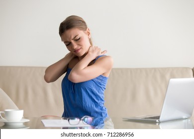 Tired woman feeling neck pain, massaging tense muscles, suffering from chronic shoulder back ache after long work on laptop computer at home, sedentary work, incorrect posture problems, fibromyalgia