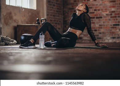 Tired woman having rest after workout. Tired and exhausted female athlete sitting on floor at gym with a water bottle. - Shutterstock ID 1145563982