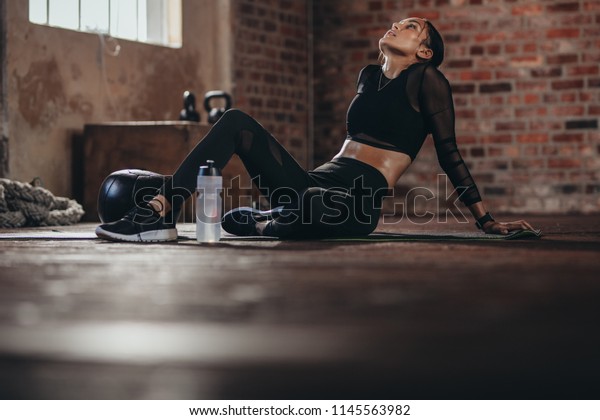 Tired woman\
having rest after workout. Tired and exhausted female athlete\
sitting on floor at gym with a water\
bottle.